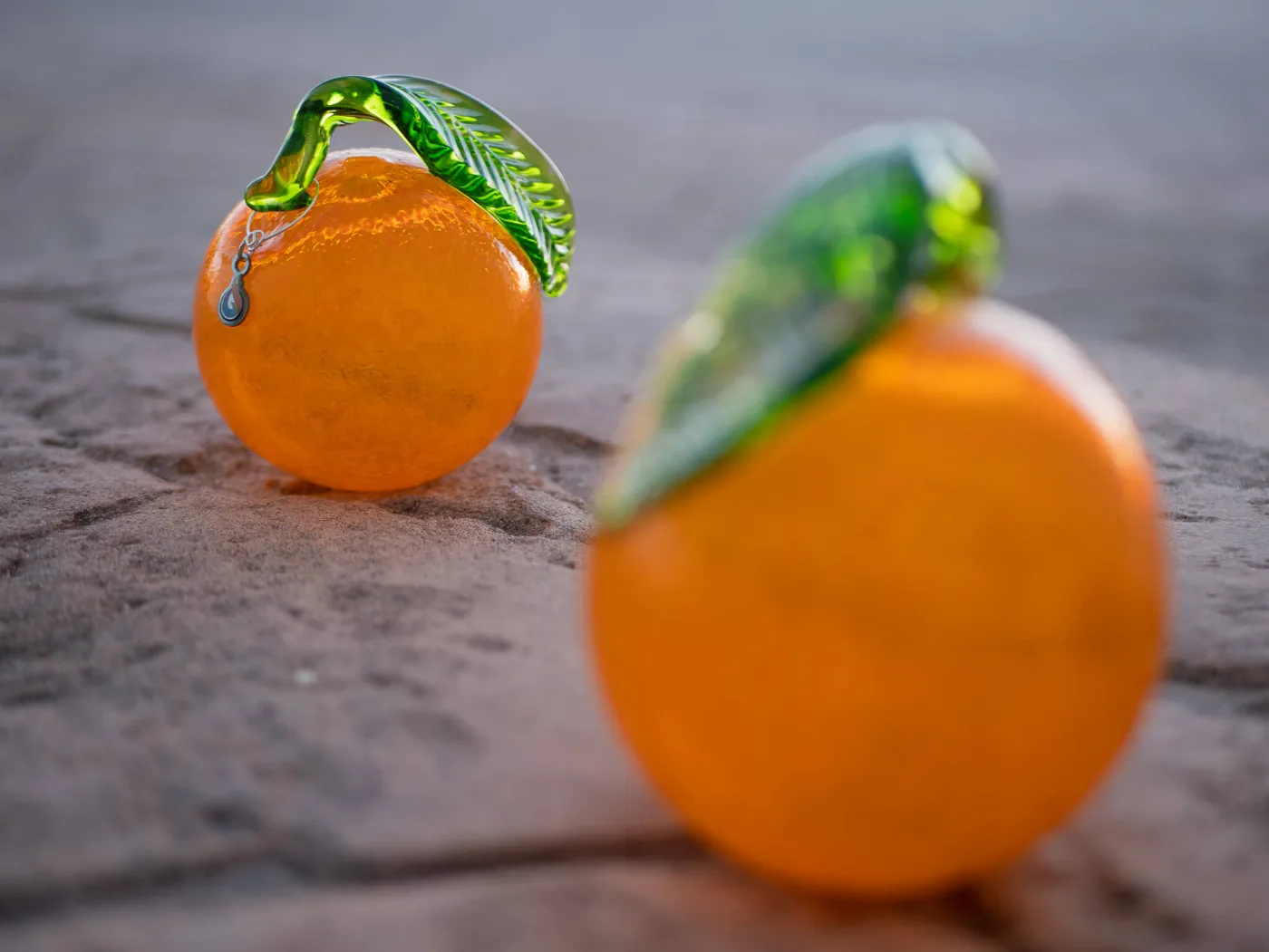 Two handblown orange glass sculptures with green leaves