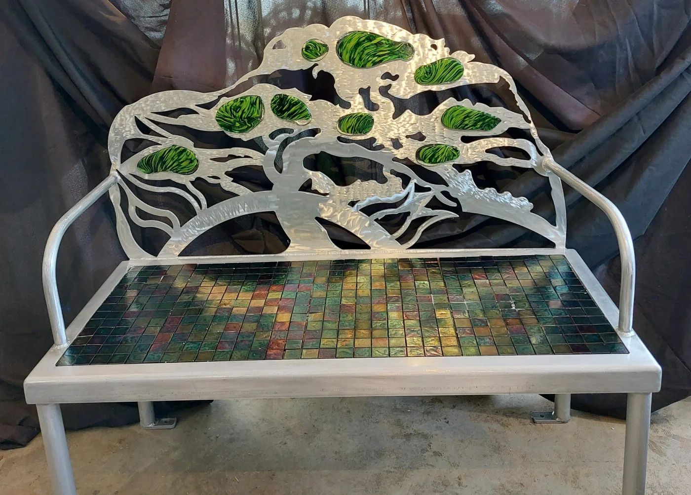 A metal art bench with green glass details and an iridescent mosaic seat